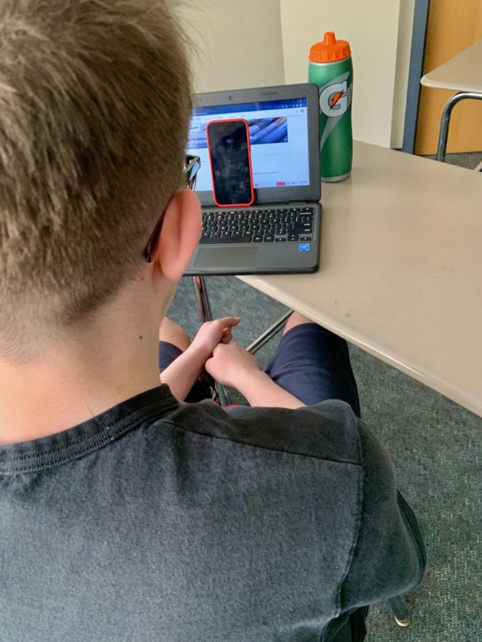 A student sneaks their cellphone behind their Chromebook